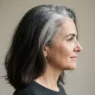 Side view of a woman in her fifties with dark brunette lengths and strong silver root regrowth showing grey transition demarcation line