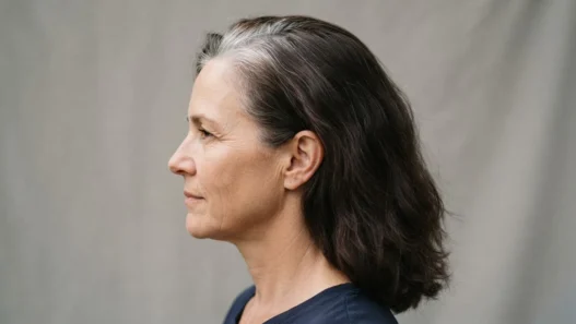 Side view of a woman in her fifties showing stark demarcation line between silver root regrowth and dark brown dyed lengths