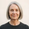Woman with fine ash grey hair in a polished blunt jaw-length bob against warm white backdrop with soft overhead light