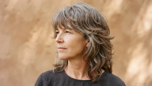 55-year-old woman with greying auburn modern shag, rough-dried to natural fall against warm clay backdrop in side light