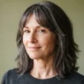 Woman in her early fifties with a mid-length lob and feathered side-swept bangs blending into layers against a sage backdrop