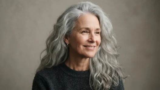 Older woman with long thick silver hair worn loose past the collarbone against a taupe backdrop in soft light