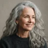 Older woman with long thick silver hair worn loose past the collarbone against a taupe backdrop in soft light