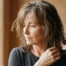 55-year-old woman with damp greying auburn hair examining shoulder-length perimeter weight before cutting shag layers