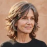 Woman aged 55 with a modern pixie shag in greying auburn hair shown in three quarter view against clay backdrop with side lighting
