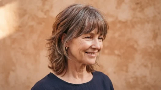 Three quarter view of a 55-year-old woman with a modern short shag in greying auburn against a warm clay backdrop