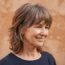 Three quarter view of a 55-year-old woman with a modern short shag in greying auburn against a warm clay backdrop