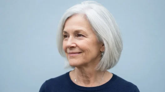 64-year-old woman with bright silver jaw-length bob against cool pale blue backdrop in documentary lighting