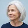 64-year-old woman with bright silver jaw-length bob against cool pale blue backdrop in documentary lighting