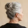 Rear three-quarter view of silver-haired woman in a pinned occasion updo against champagne backdrop with warm soft light