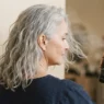 Silver-haired woman over 60 having texturizing spray misted through back hair panel before styling