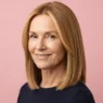 Woman in her late fifties with warm honey-blonde blunt lob to the collarbone showing even golden tones against soft pink backdrop