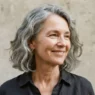 Sixty-year-old woman with square jaw and wavy grey lob against stone backdrop, wave sitting at jaw level